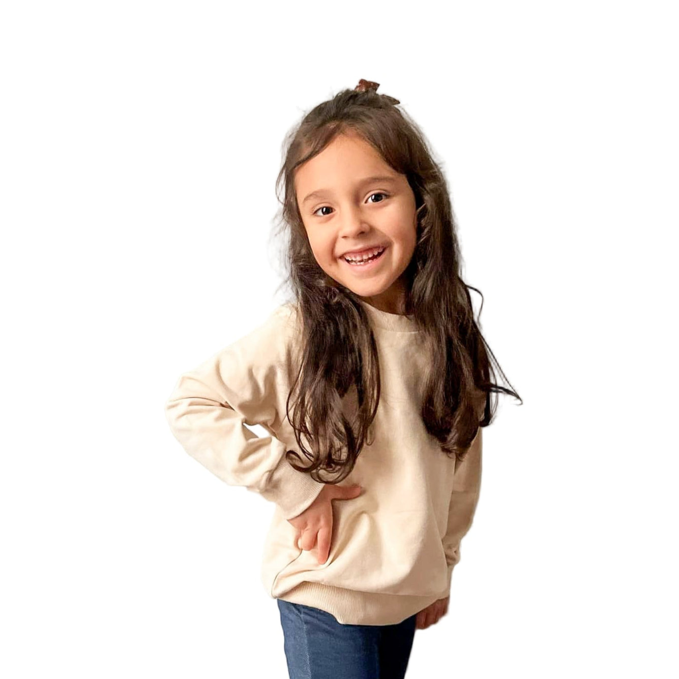 A child wearing a beige organic cotton pullover and blue jeans standing against a white background.
